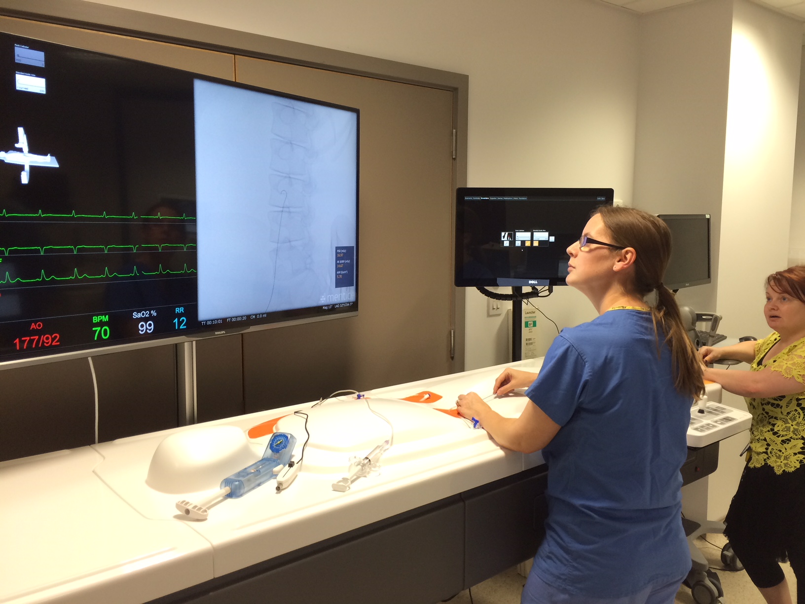 Simulated endovascular procedure showing a fluoroscopy display and vital signs monitor