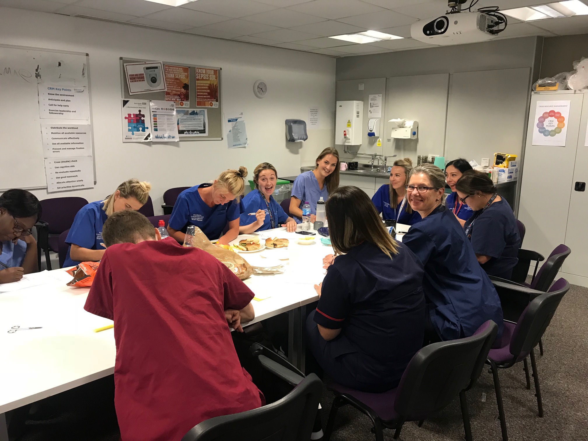 Simulation faculty and clinical staff gathered around a table during a course debrief
