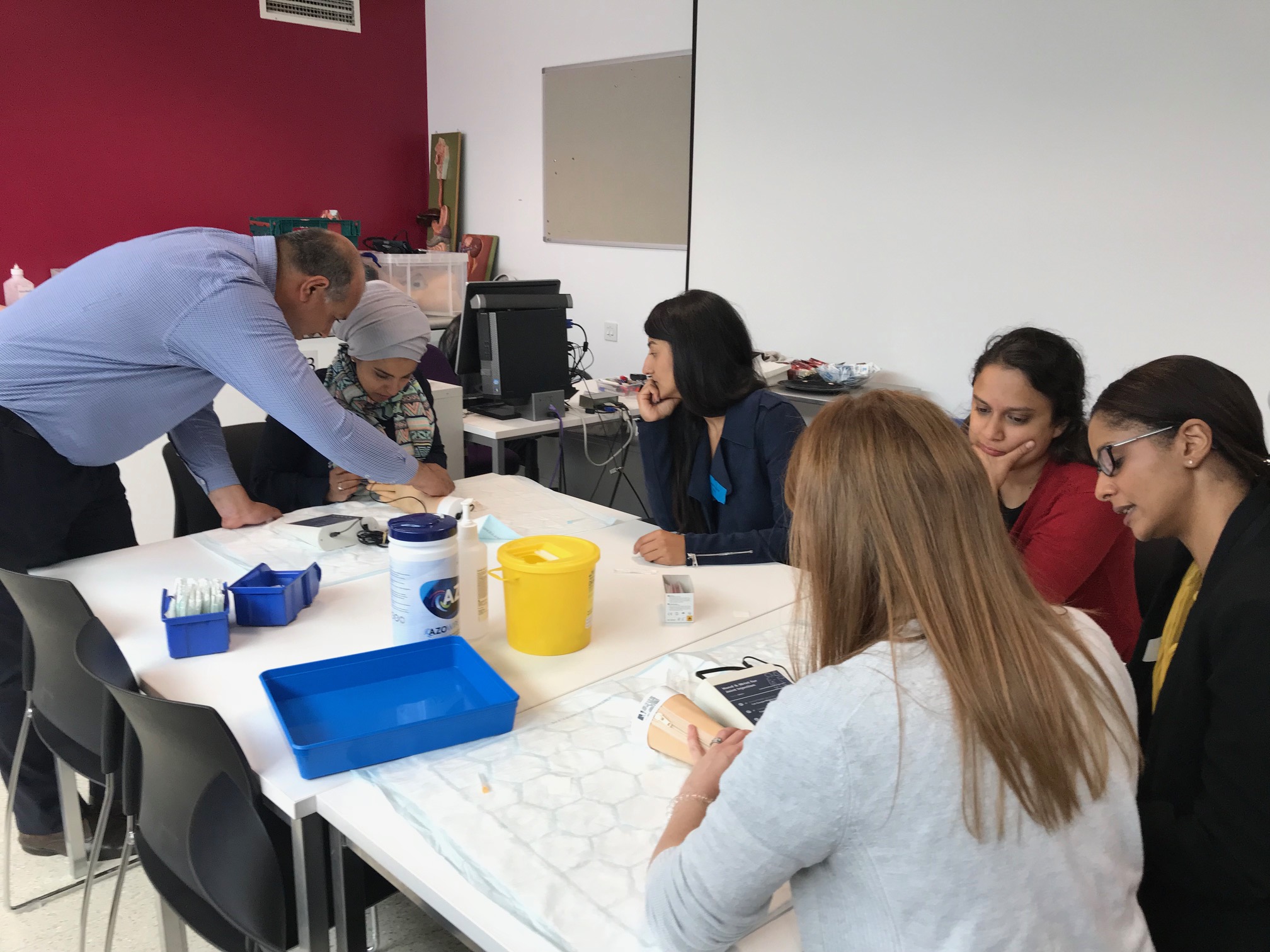 Faculty and candidates practising suturing technique around a table during a workshop